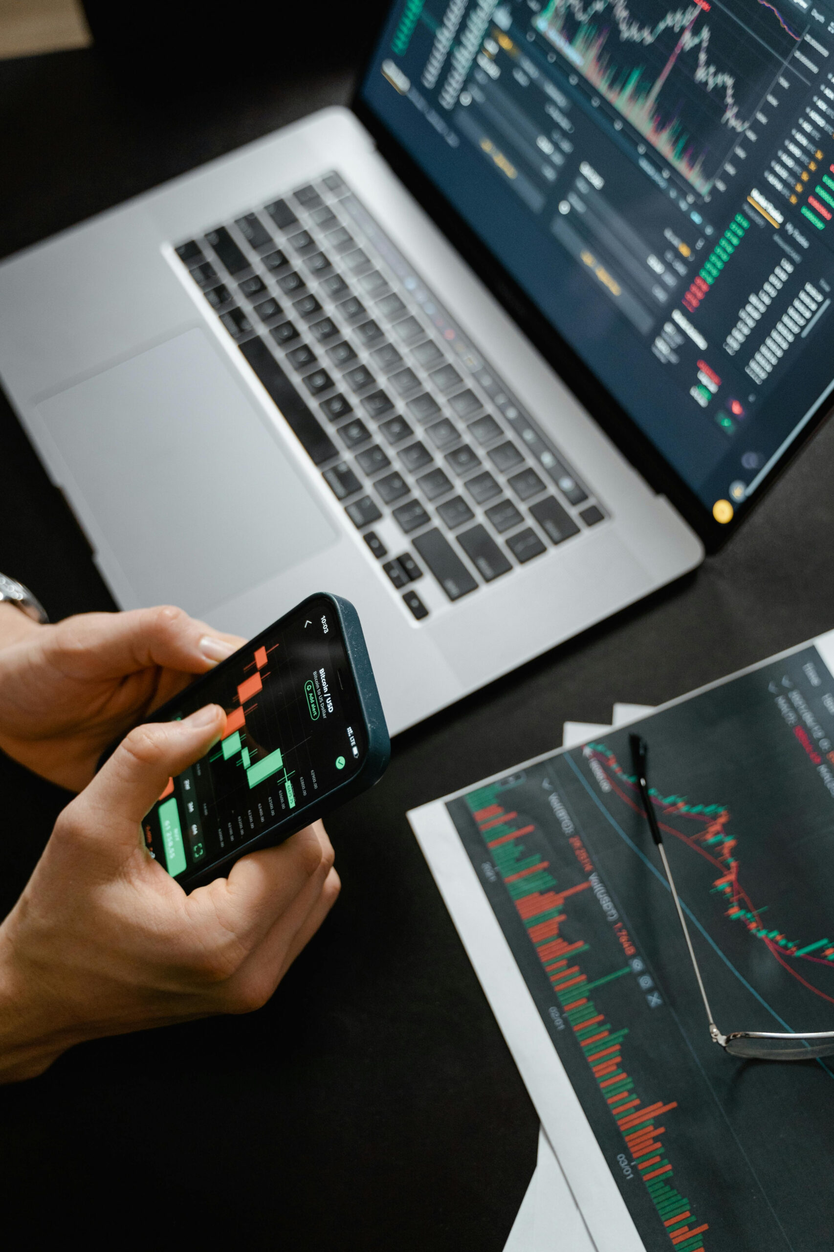 Person using a smartphone and laptop to view financial charts